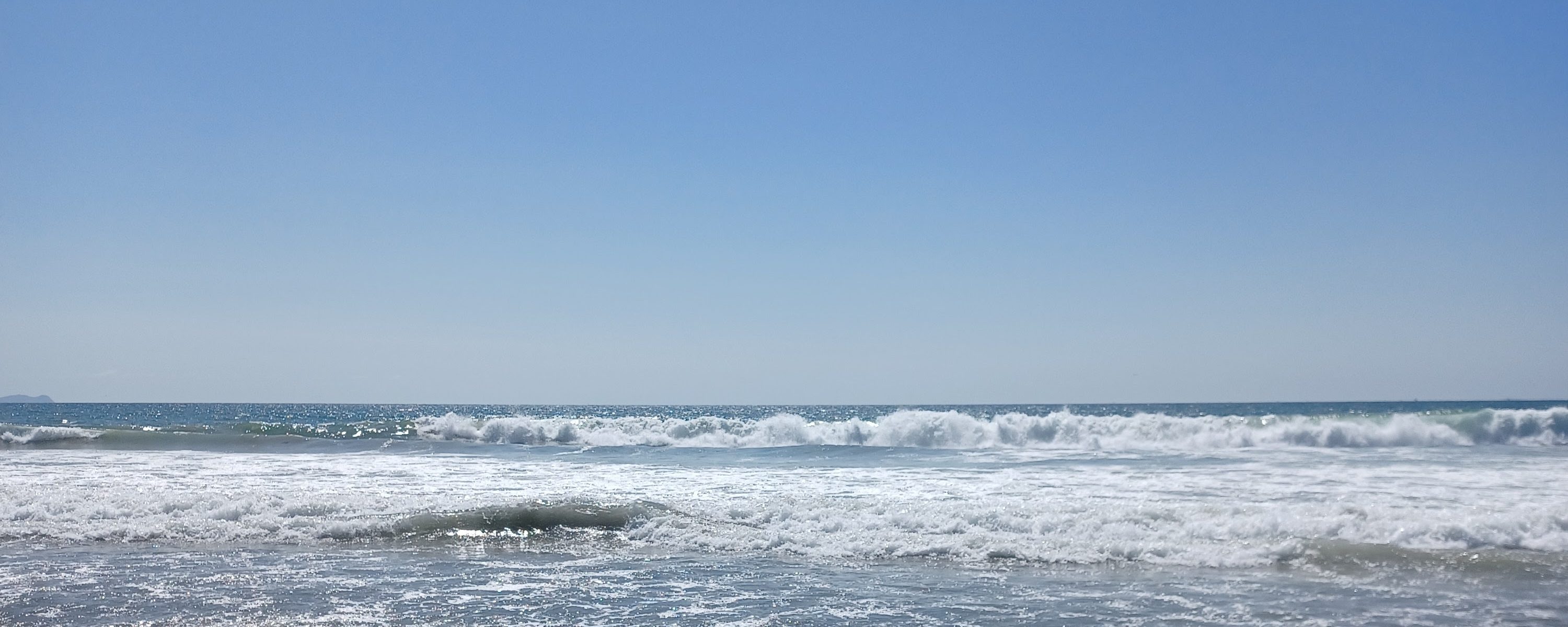 Waves breaking on a Pacific shoreline under a clear sky